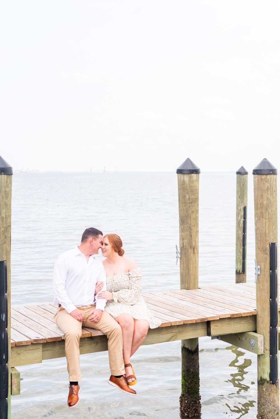 engaged couple sit on dock together during engagement photos in Virginia